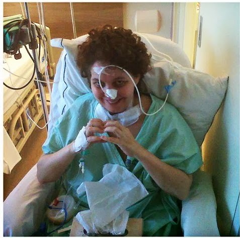 Melissa no hospital durante o tratamento, fazendo um coração com as mãos